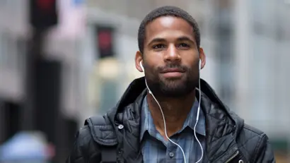 A man wearing a black jacket and ear buds looking into the distance 